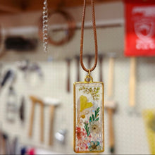 Load image into Gallery viewer, Decorative pendant with floral and resin design held by a hand in an indoor setting.