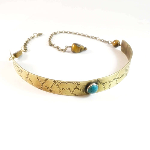 A brass metal choker necklace with a turquoise bezel as the center piece, featuring hand stamp pattern detailing.